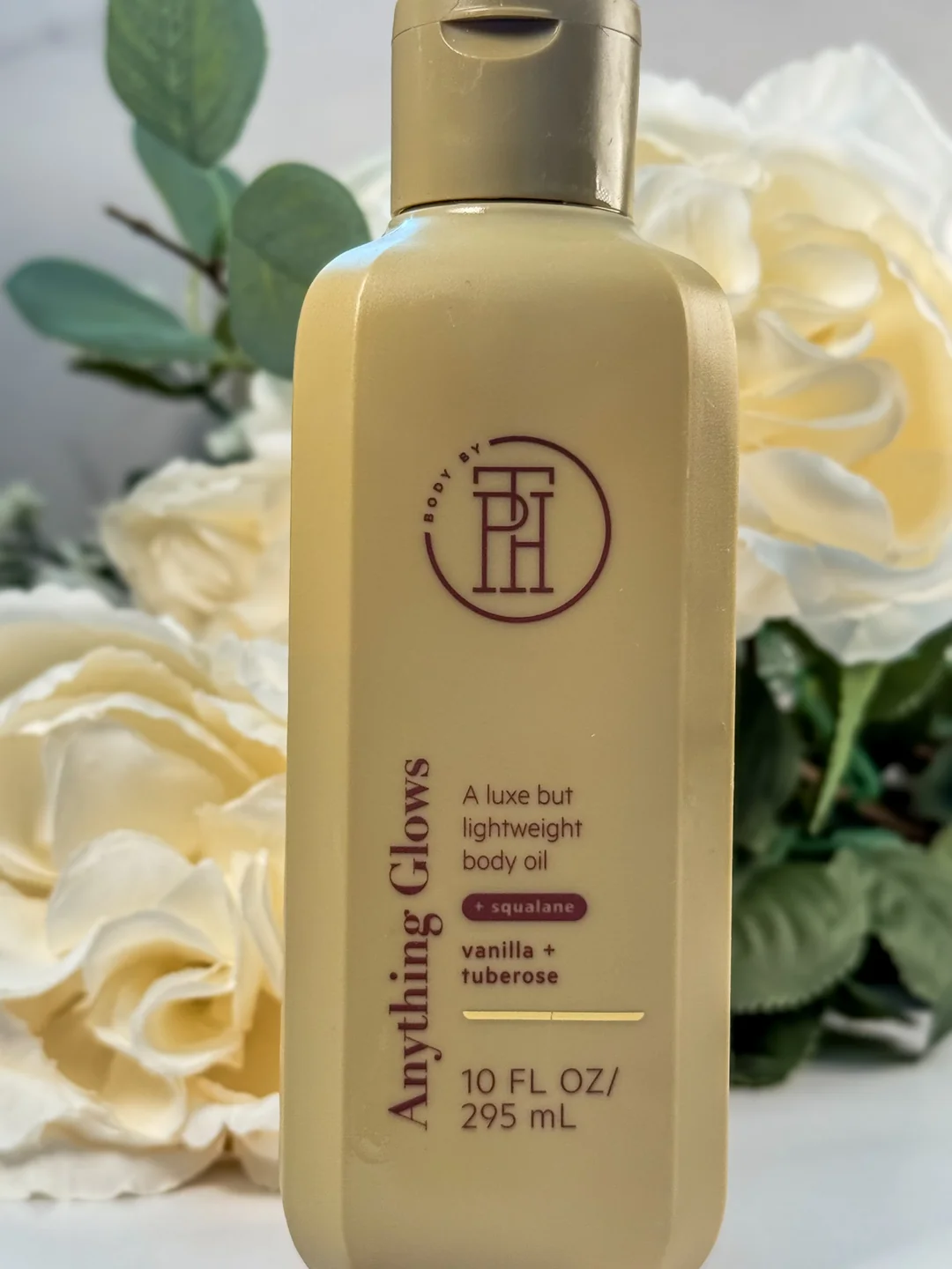 Body By PH Anything Glows vanilla tuberose body oil photographed among ivory white roses.