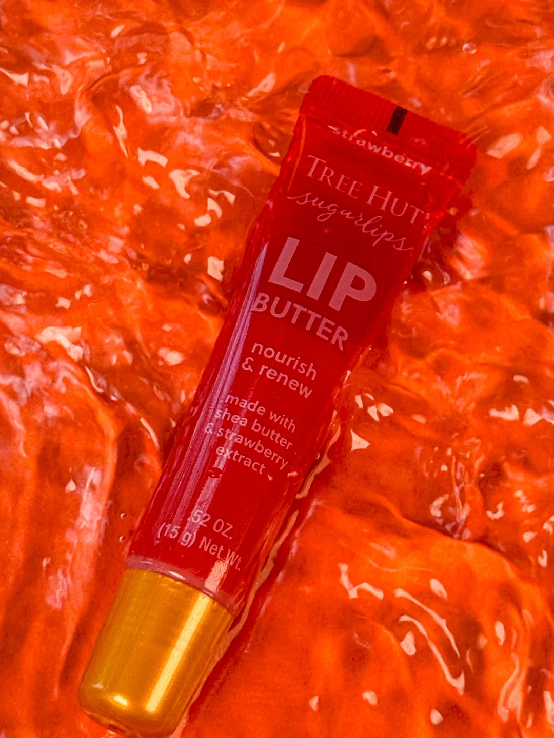 Tree Hut Sugarlips Lip Butter in red packaging surrounded by vivid strawberry red glossy textures.