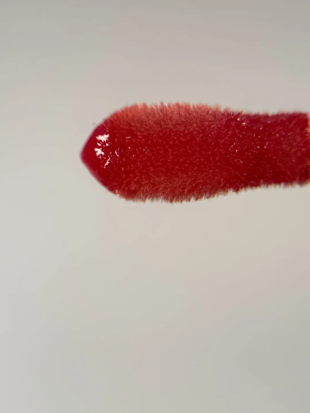 Macro close-up of a red glossy lip product applicator against a light background.